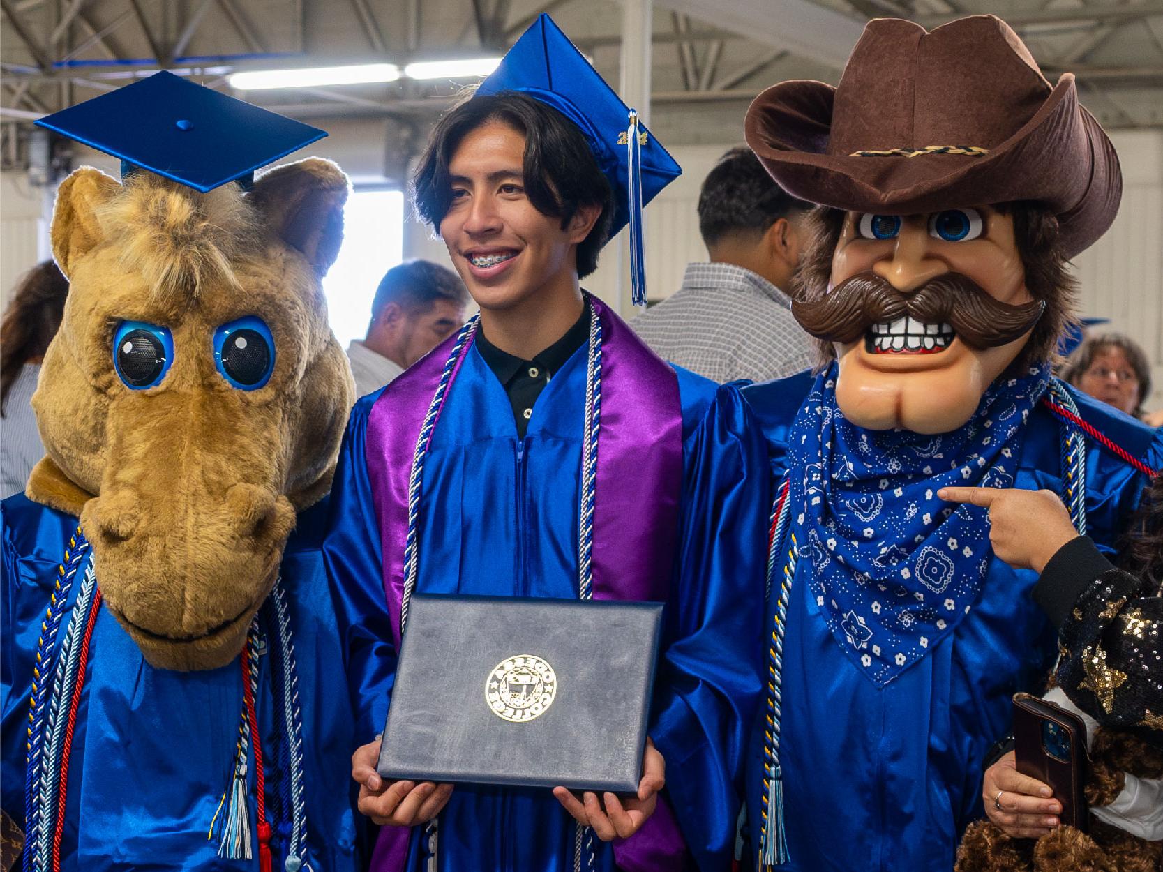 Male Graduate Posing with Willie the Wrangler and Bullseye Billie Mascots